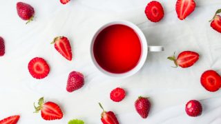 A cup of strawberry tea, whole and sliced strawberries on a white counter.