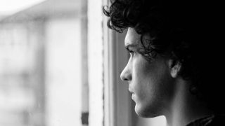 A young man looking out of a window with a subdued expression