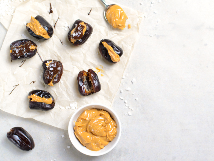 Dates with peanut butter filling, dark chocolate, and sea salt on a white counter