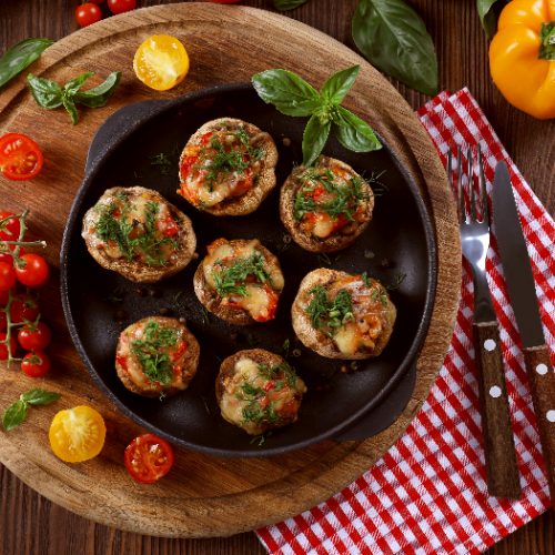 A flat lay image of a frying pan with stuffed mushrooms and vegetables on the table