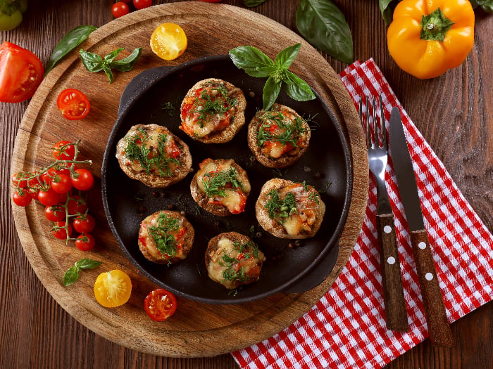 A flat lay image of a frying pan with stuffed mushrooms and vegetables on the table