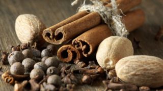 Whole spices like cinnamon sticks, whole peppers, and nutmeg on a wooden counter