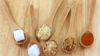 Spoons of different types of sugar such as sugar cube, types of granulated sugar, honey on wood