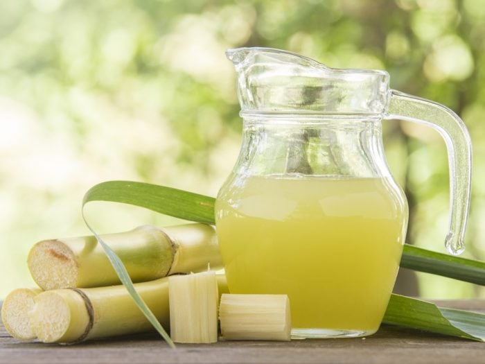 A jar of sugarcane juice with fresh halved sugarcane on a wooden table