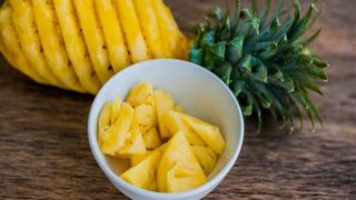 Chunks of pineapple in a bowl, placed along with a skinned whole pineapple