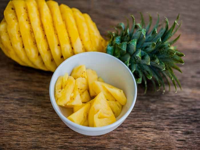 Chunks of pineapple in a bowl, placed along with a skinned whole pineapple