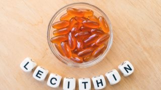 A bowl of sunflower lecithin gel capsules with the word lecithin prepared with plastic alphabet cubes on a wooden table