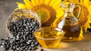 A bowl filled with sunflower seeds, a jar of sunflower oil and fresh sunflower flowers on a wooden table