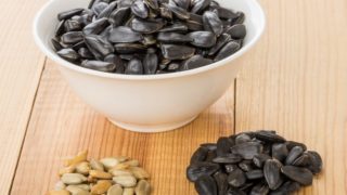 A bowl of dried sunflower seeds and peeled sunflower seeds on a wooden table