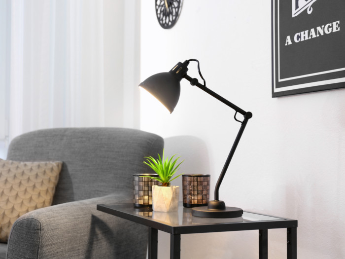 A one-seater couch next to a side table with a lamp and a plant on it