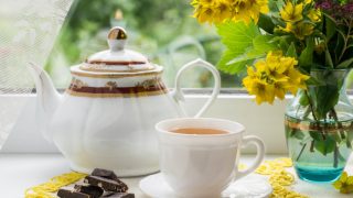 A tea set with black tea in a teacup, chocolate, and fresh flowers