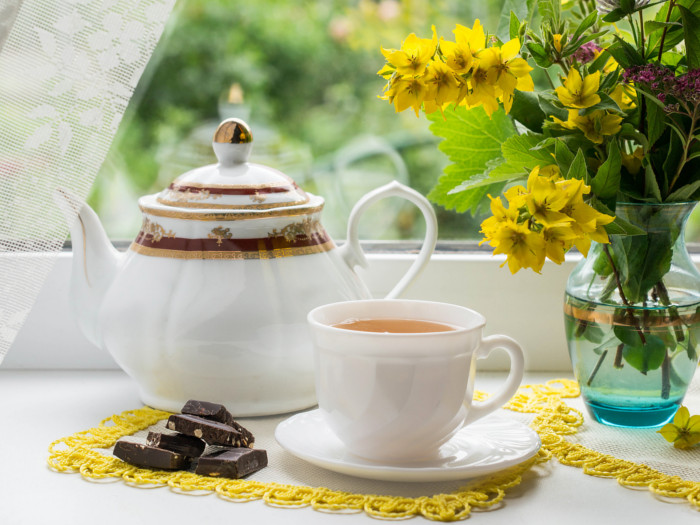 A tea set with black tea in a teacup, chocolate, and fresh flowers