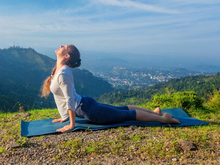 A lady performing surya namaskar on a mountain