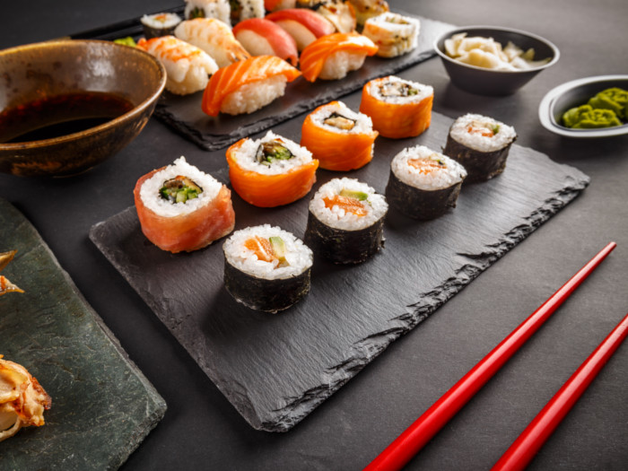 A palate of different sushi rolls with chopsticks wasabi, soy sauce on black table