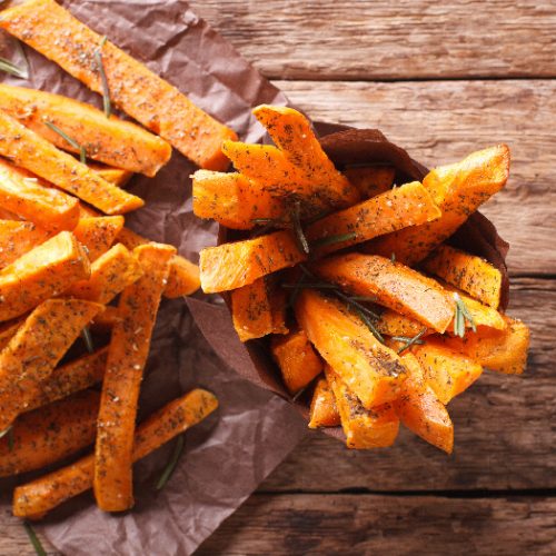 Sweet potato fries with ketchup on parchment paper and wood