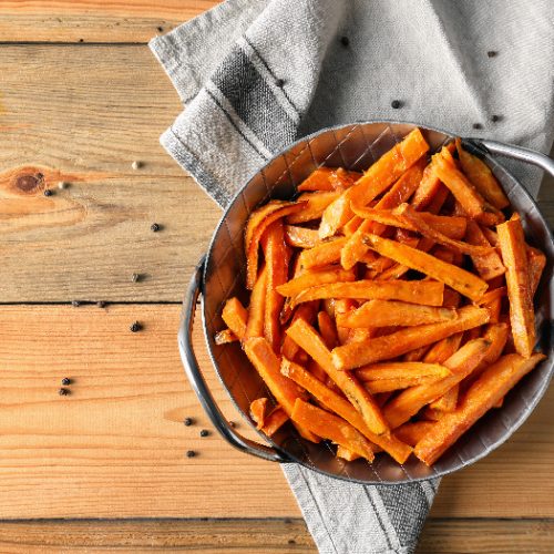 Sweet potato fries in a bowl on a napkin on a wooden table