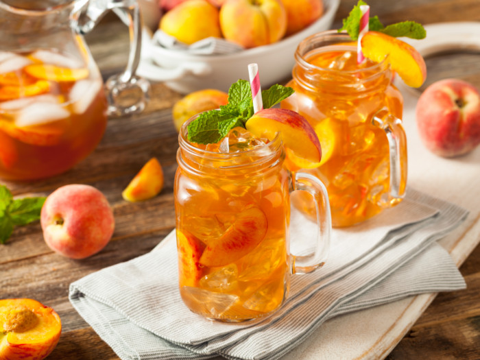 Sweet tea flavored with fresh peach in mason jars and a pitcher, with peaches on a table