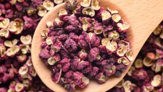 A close-up shot of a wooden spoon carrying Szechuan pepper