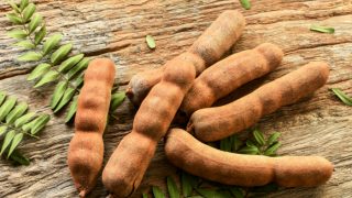 Sweet ripe tamarind pods with leaflets on a wooden background