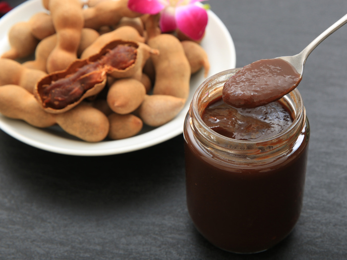 Tamarind chutney in a jar with a spoon next to a plate of whole tamarind