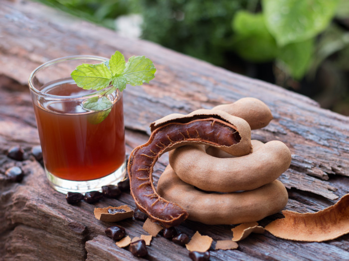 A small glass of tamarind juice and three tamarind pods on a table