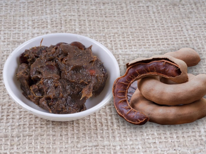 White bowl of tamarind paste and tamarind pods placed on burlap cloth.