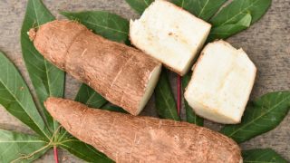 Whole and halved raw tapioca with leaves on a wooden table