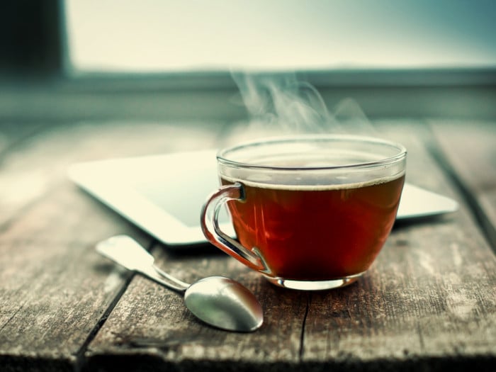 A cup of hot tea with a spoon and plate on a wooden table