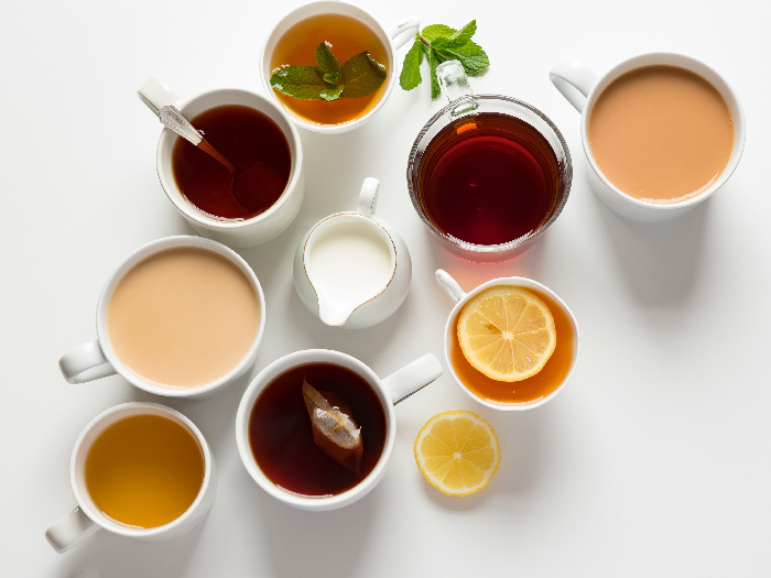 Flat lay of various black, milk, and green teas in cups on a white background