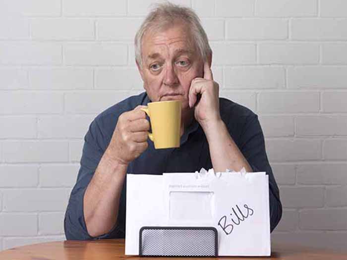 An older man holding a yellow cup, looking distressed with a folder labeled 'Bills'