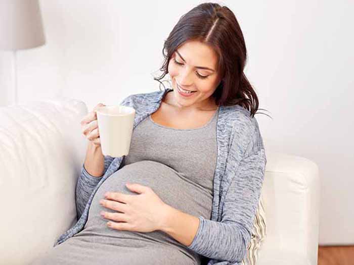 Pregnant woman holding a cup of tea in one hand.