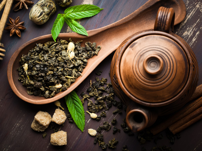 Top view of tea leaves in a wooden spoon with a wood teapot next to it