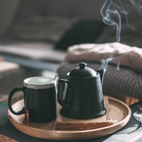 A steaming cup of tea and a pot on a table
