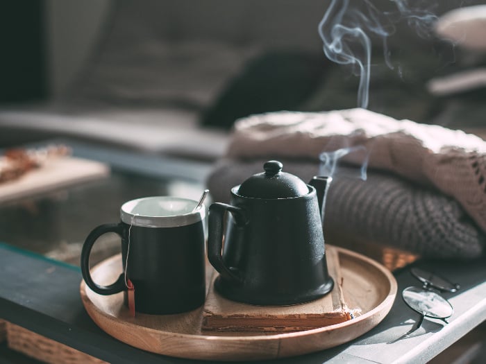 A steaming cup of tea and a pot on a table