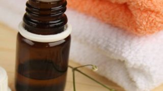 A bottle of essential oil kept next to a pile of white and orange colored towels