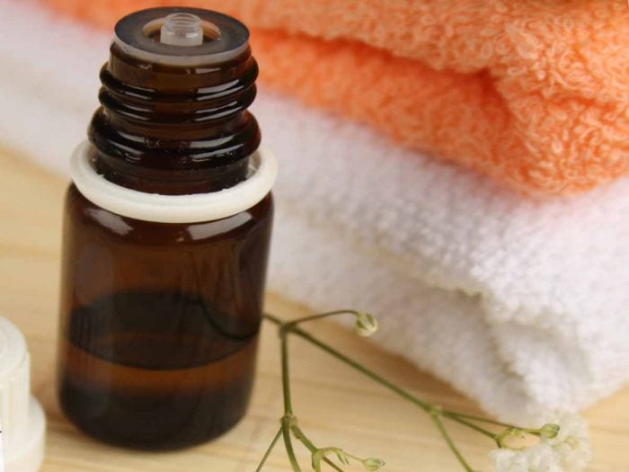 A bottle of essential oil kept next to a pile of white and orange colored towels