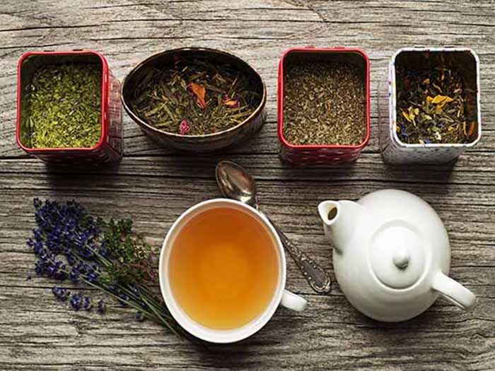 Different types of loose leaf tea leaves in bowls with a teapot and teacup