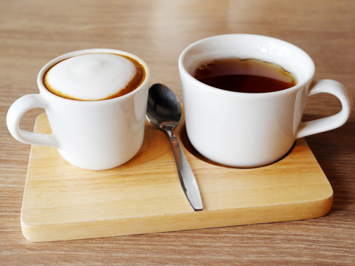 Cups of tea and coffee with a single silver spoon on a wooden tray