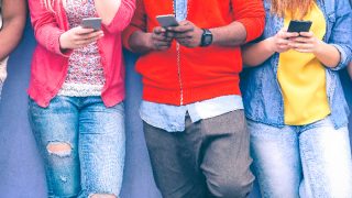 Teenagers texting mobile phone messages leaning on wall