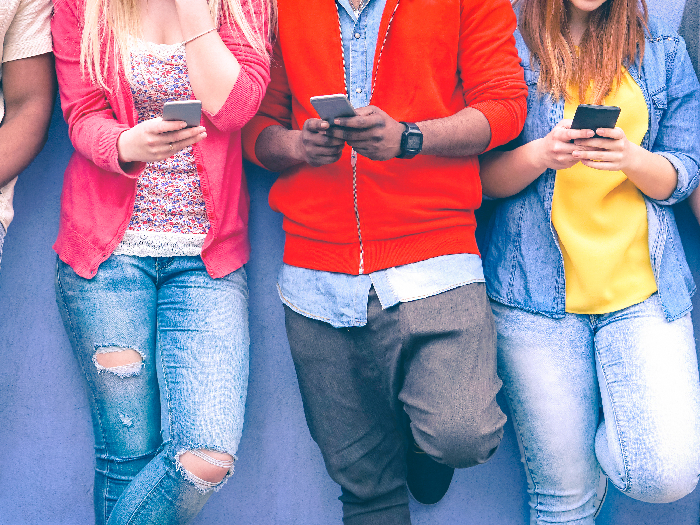 Adolescents texting mobile phone messages leaning on wall