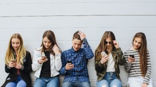 A group of teenagers sitting outdoors using their mobile phones