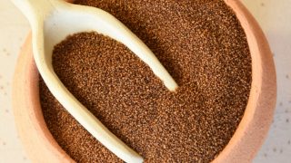 A rustic pottery bowl with a handmade ceramic scoop of teff grains on a white background