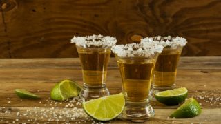 Three tequila glasses kept atop a wooden table with lemon slices cut and kept next to the glasses