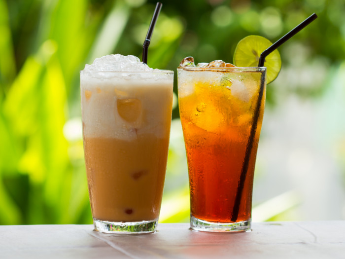 Two glasses of iced tea next to each against a green background