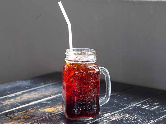 A glass jar filled with Thai iced tea kept atop a black table against a grey background