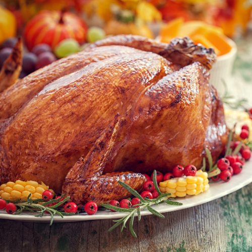 Thanksgiving turkey with corn and cranberries on a white plate and squash in the background