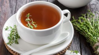 A white cup of thyme tea with sugar cubes and thyme herb on a wooden background