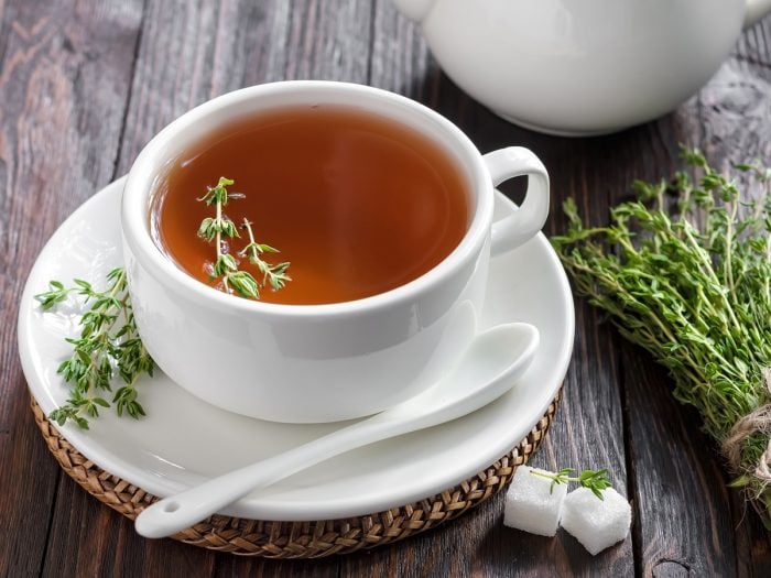 A white cup of thyme tea with sugar cubes and thyme herb on a wooden background