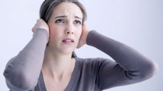 A young woman suffering from tinnitus covering her ears with her hands