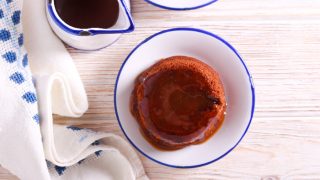 Top view of sticky toffee pudding in a white and blue bowl with a small jug of toffee sauce